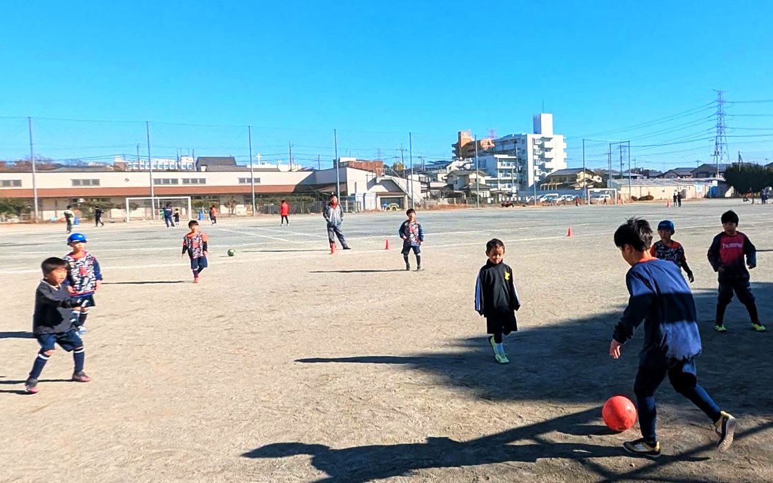 青空の下、グラウンドでボールを使って練習する子どもたち